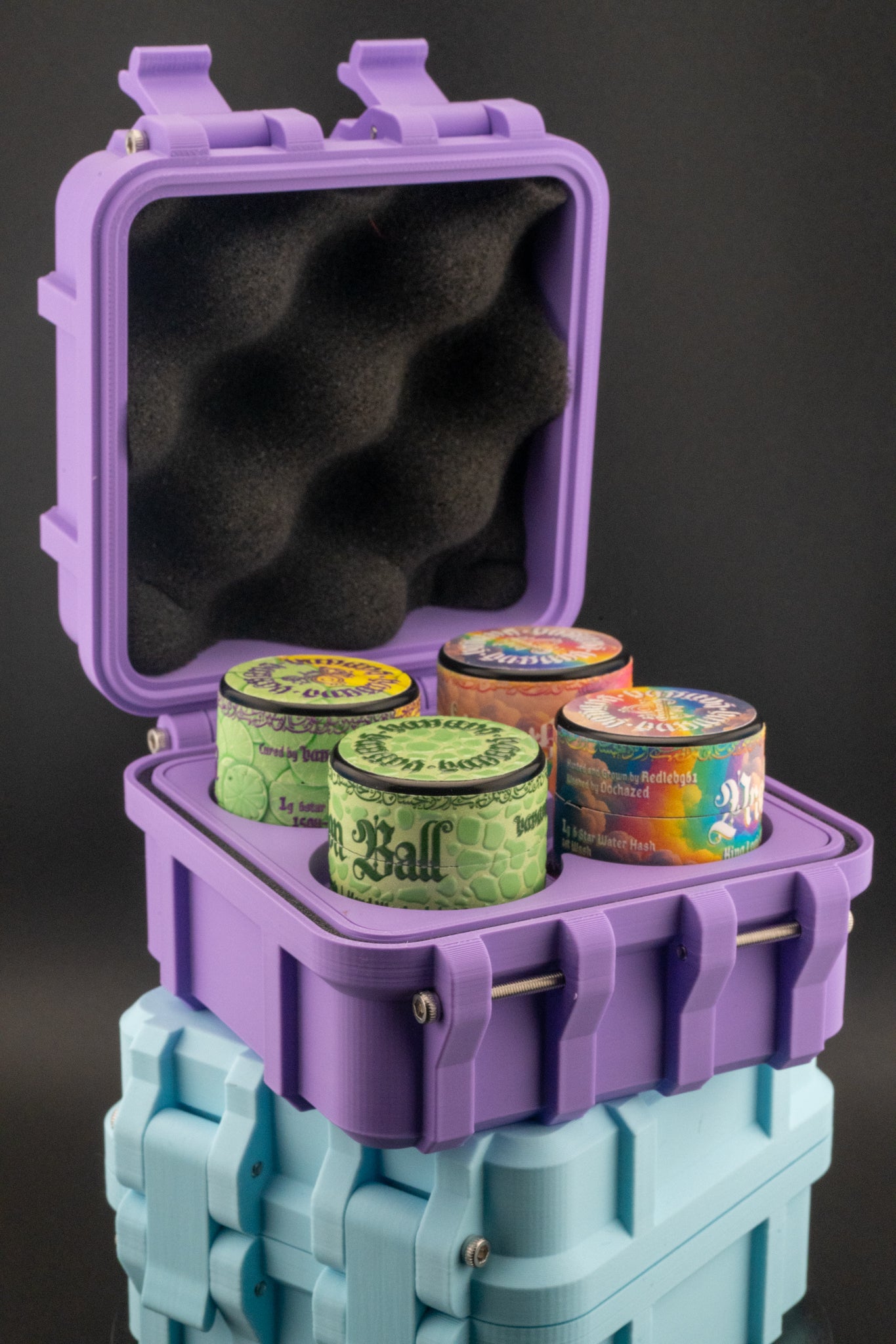 Purple case with black interior holding colorful containers, stacked on a blue block against a dark background.